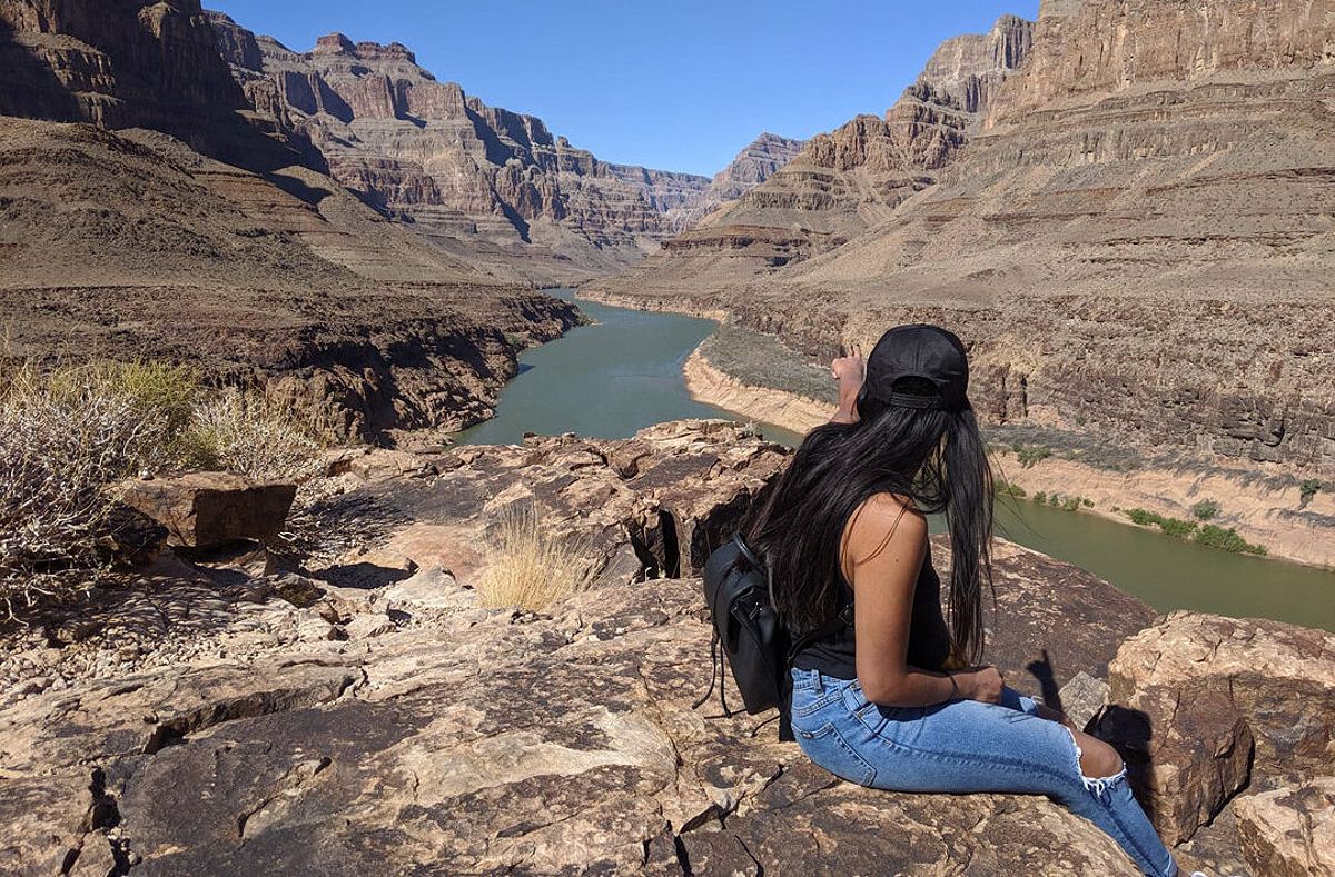 A solo female traveler sitting on a cliff overlooking the grand canyon.