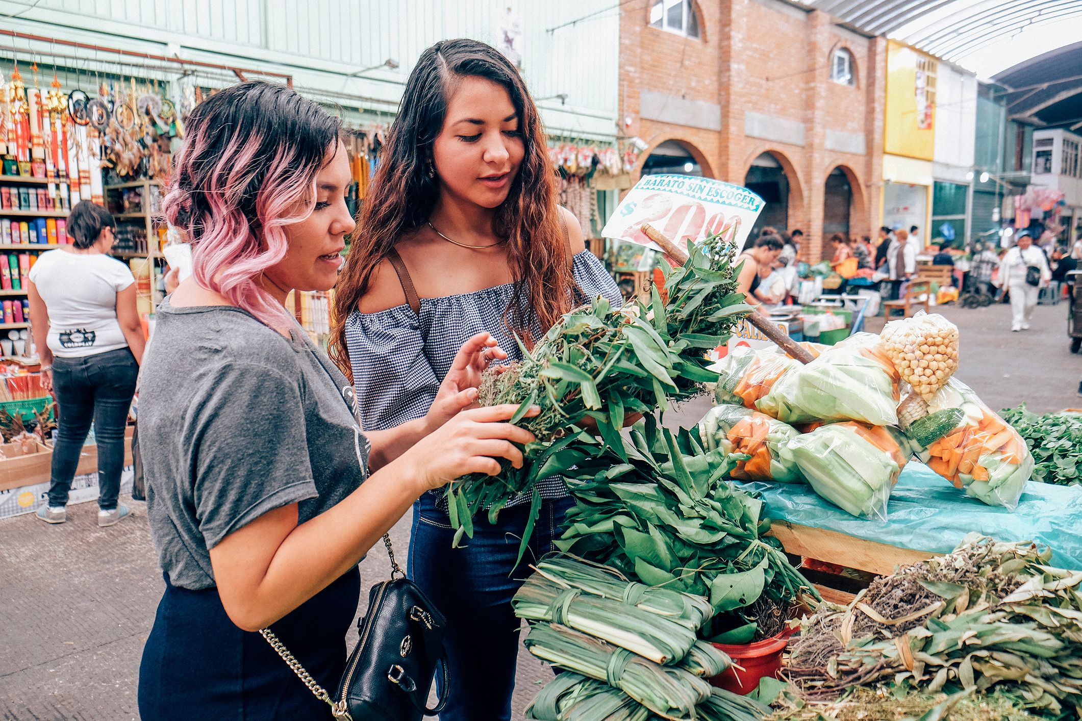 Two women friends looking at vegetables in an open-air market in Mexico City